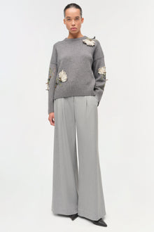 Gray knit sweater with cream floral embellishments on shoulders and sleeves, paired with gray wide-leg trousers.