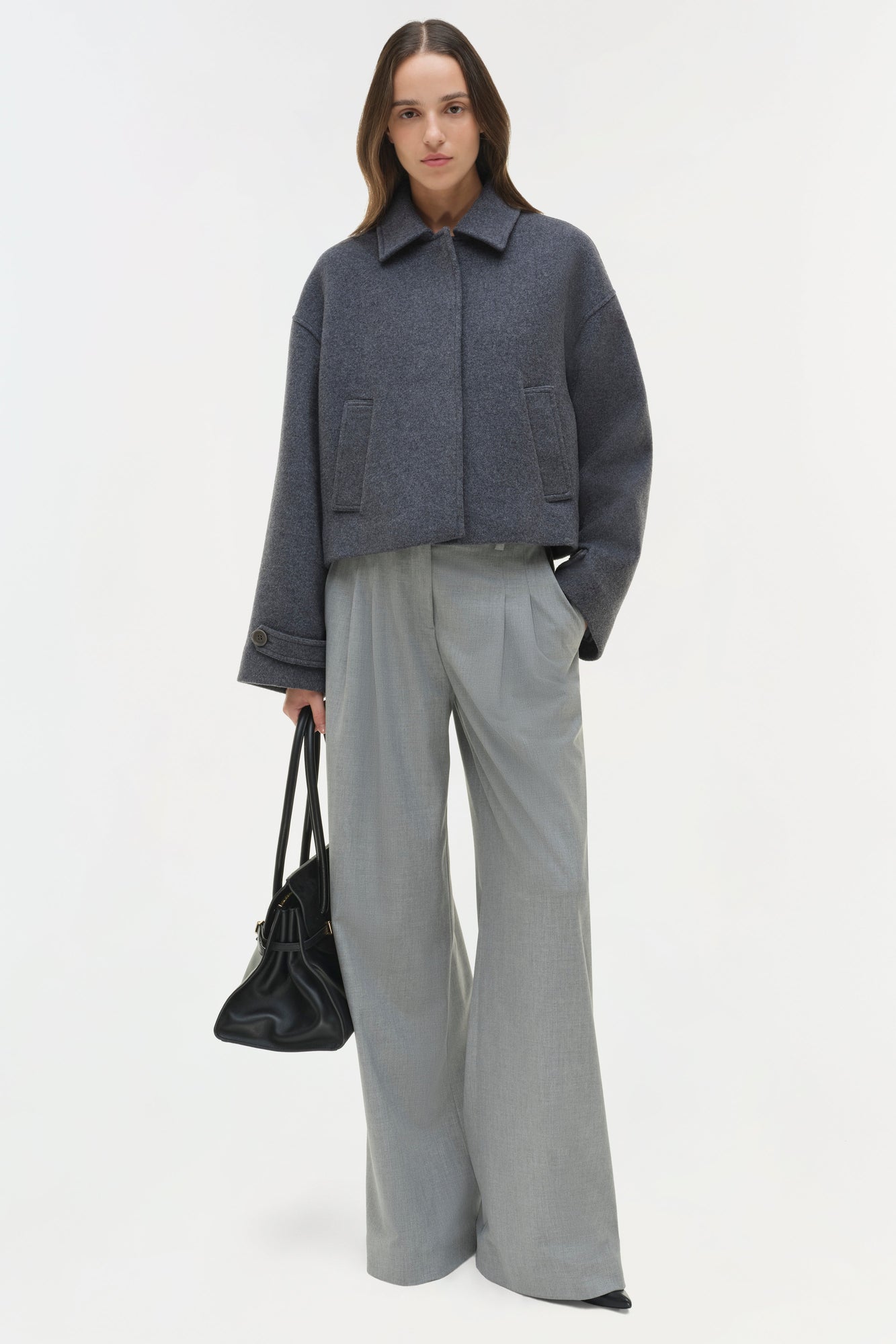Charcoal wool jacket with pointed collar, front button closure, and patch pockets worn with gray trousers.
