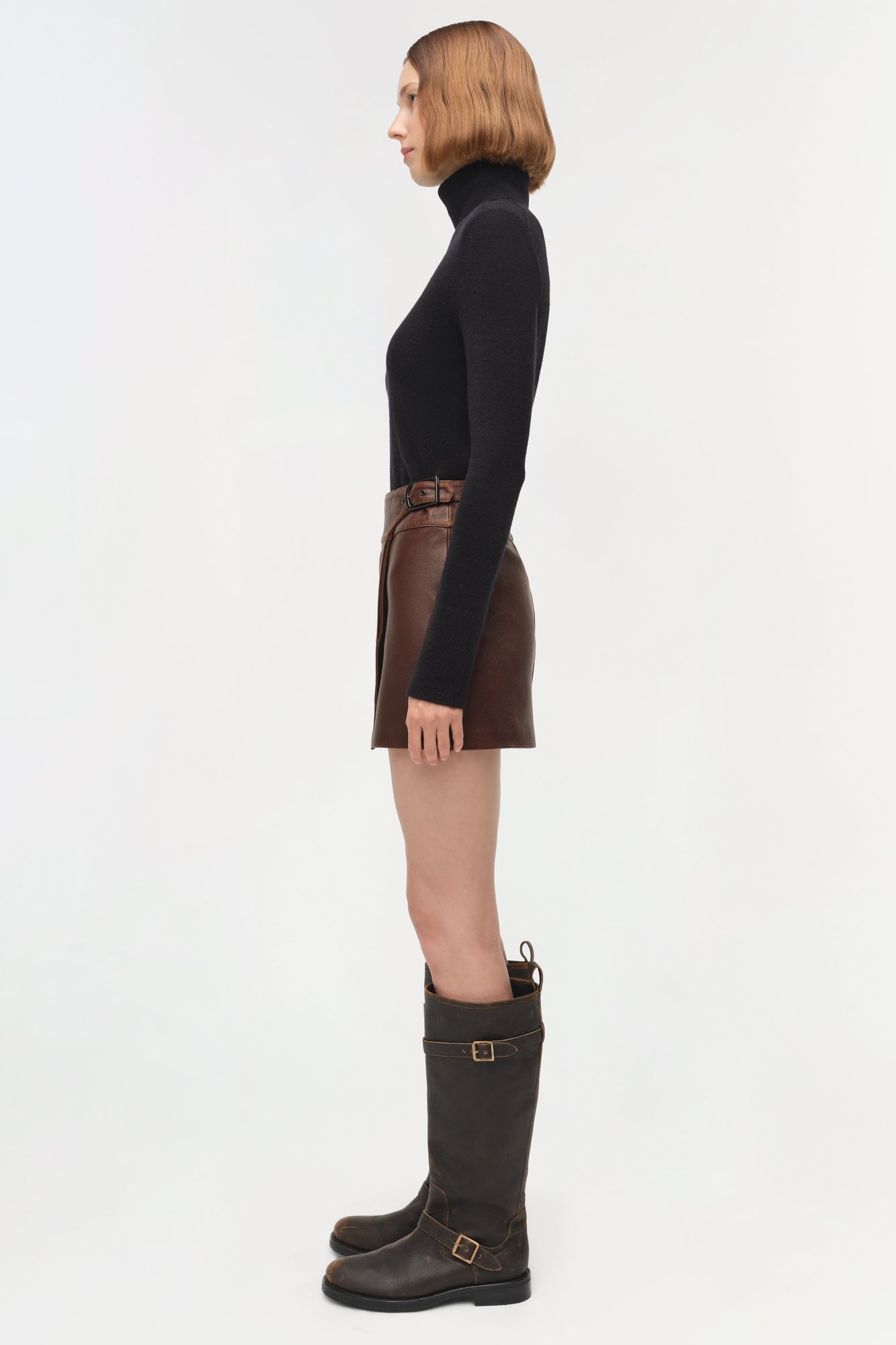 Brown leather mini skirt with buckle waistband detail, worn with black turtleneck.