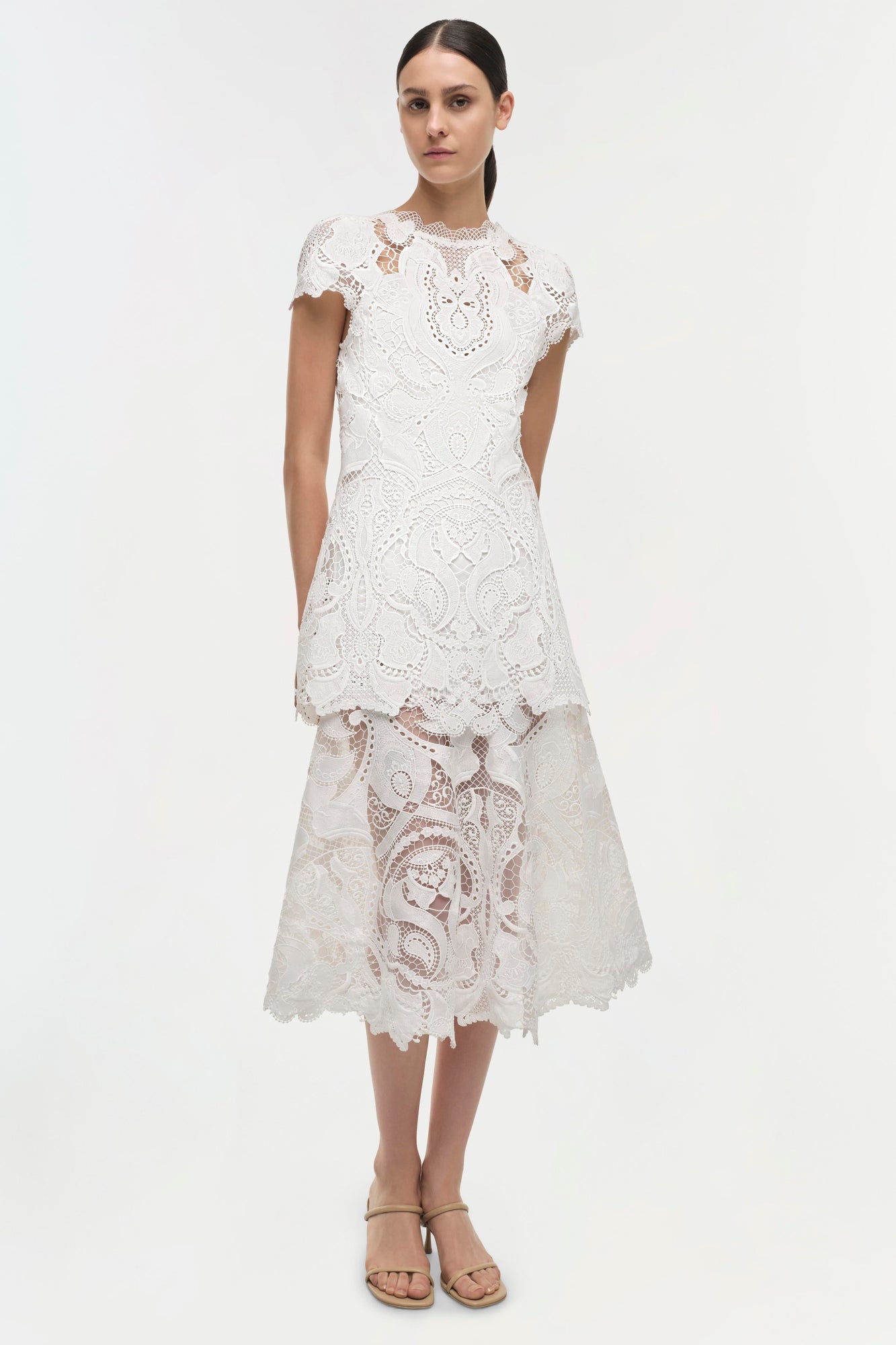 White lace dress with short sleeves, patterned cutout details, and layered midi skirt with scalloped hem.