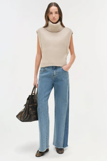 Woman wearing light blue straight leg jeans with raw hem and cream sleeveless turtleneck sweater.
