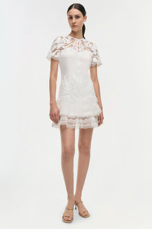 White lace dress with short flutter sleeves and tiered skirt hem, worn with tan sandals.