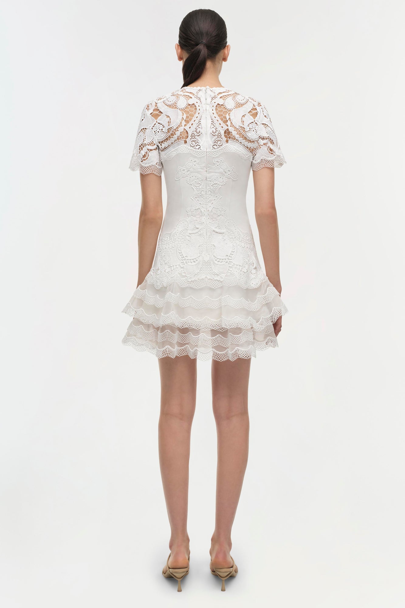 White lace dress with short sleeves, tiered ruffle skirt, and intricate lace detailing throughout, shown from back view.