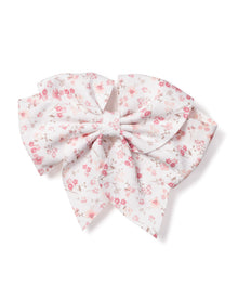 The Petite Plume Girls Dorset Floral Hair Bow features a white fabric with small pink flowers and delicate gray leaves, tied in symmetrical loops and tails. Ideal as a holiday gift or charming stocking stuffer.