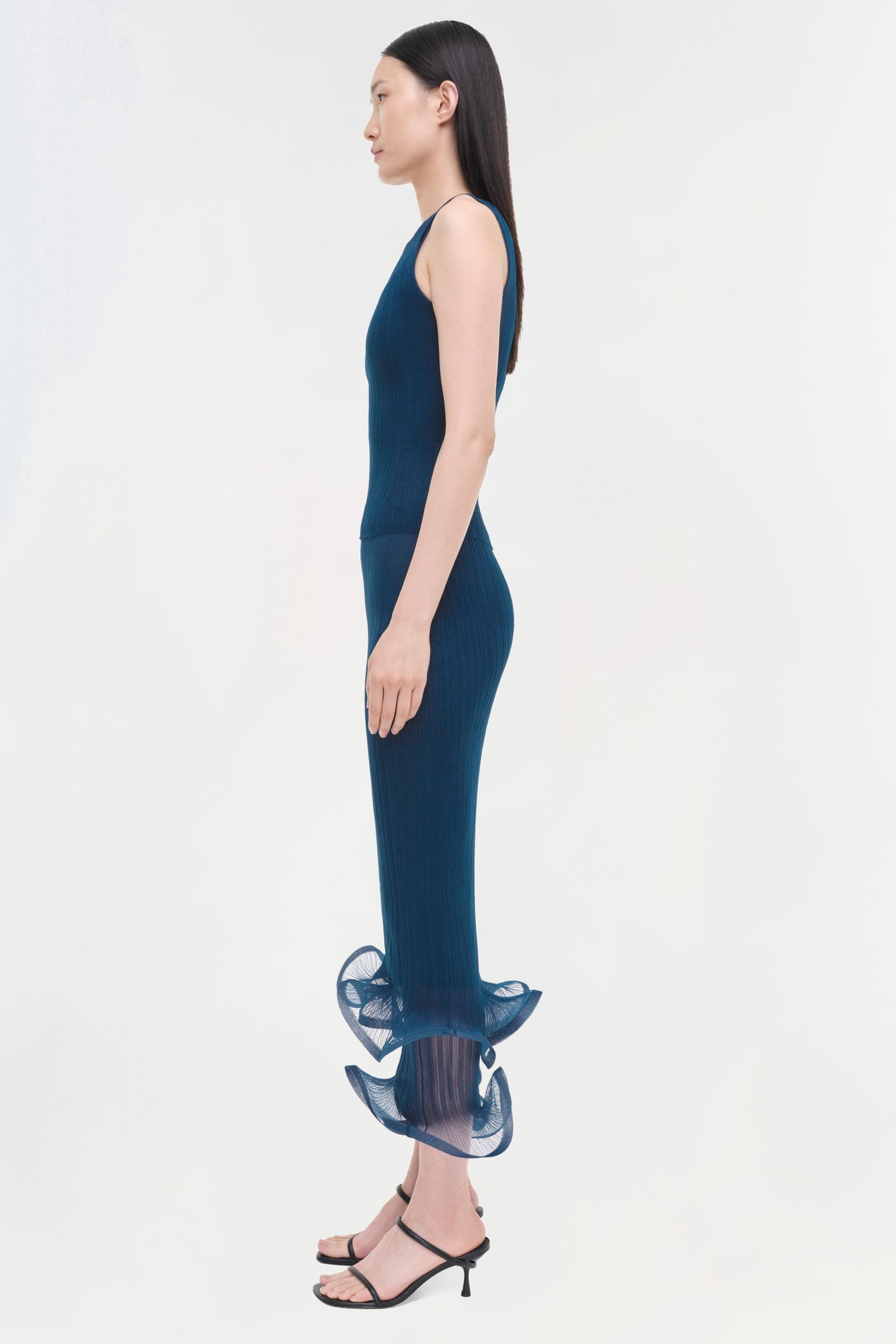 Navy ribbed sleeveless tank with pleated ruffle hem, shown on model in profile view.