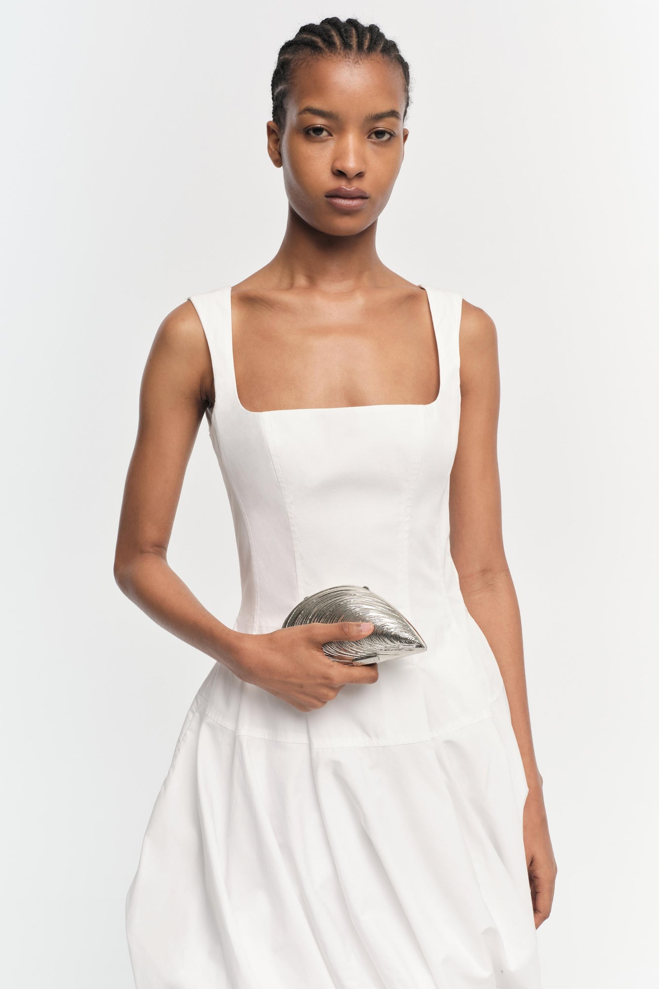 White sleeveless square-neck mini dress with full skirt, worn with silver metallic clutch.
