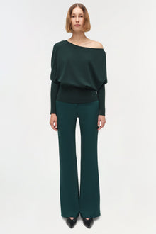 Dark green off-shoulder sweater with draped long sleeves worn with matching flared pants.