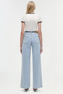 Woman wearing cream short-sleeve top with black trim and light blue jeans, shown from back view.