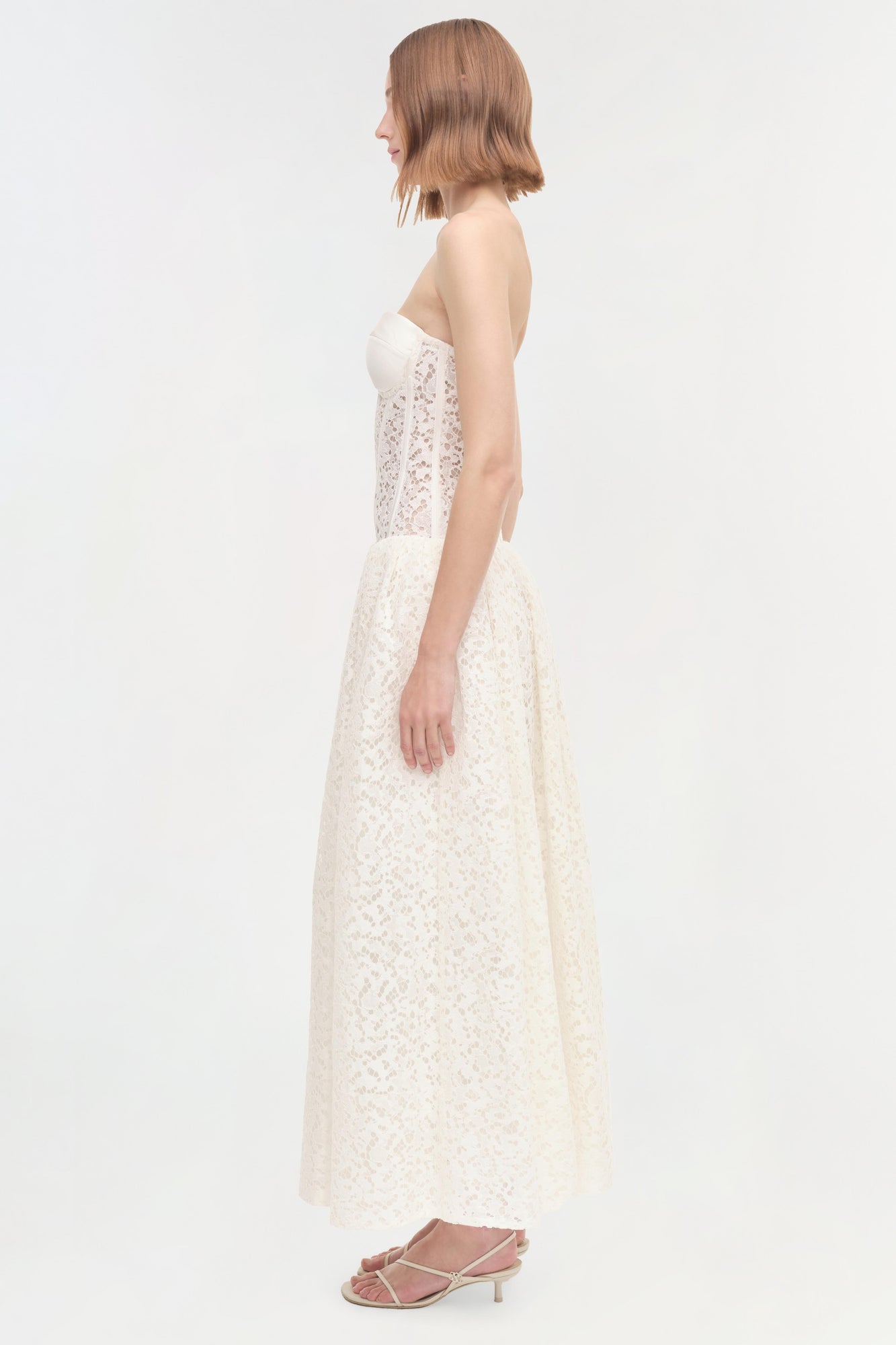 White strapless lace dress with fitted bodice and full skirt, shown from the side on a model.