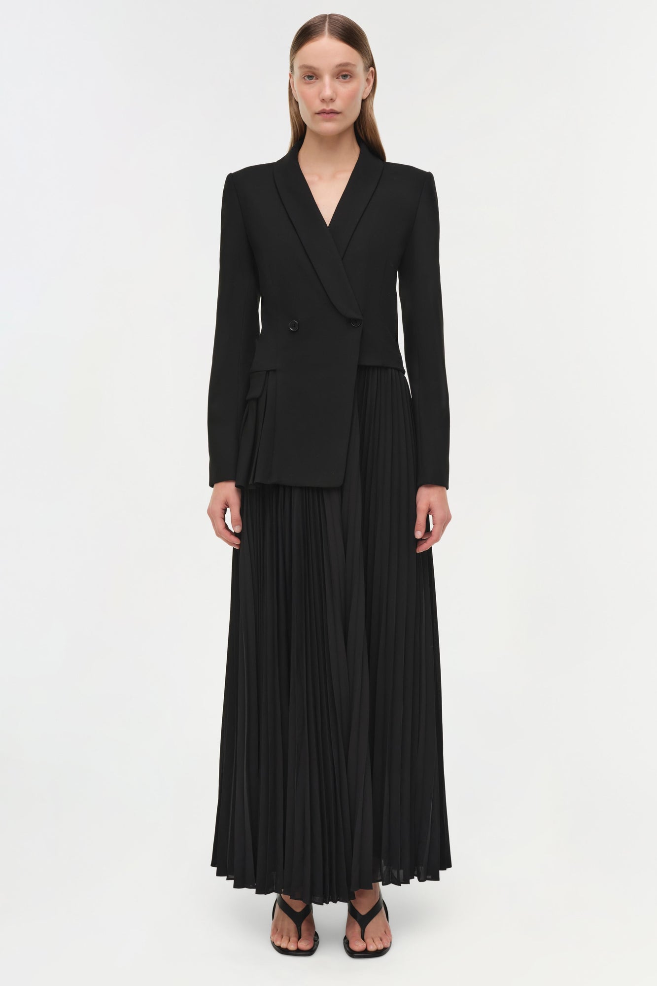 Black double-breasted blazer dress with pleated skirt extending to ankles, long sleeves, worn with black sandals.