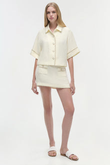 Cream textured mini skirt with front button detail and raw hemline, styled as part of a matching two-piece set.