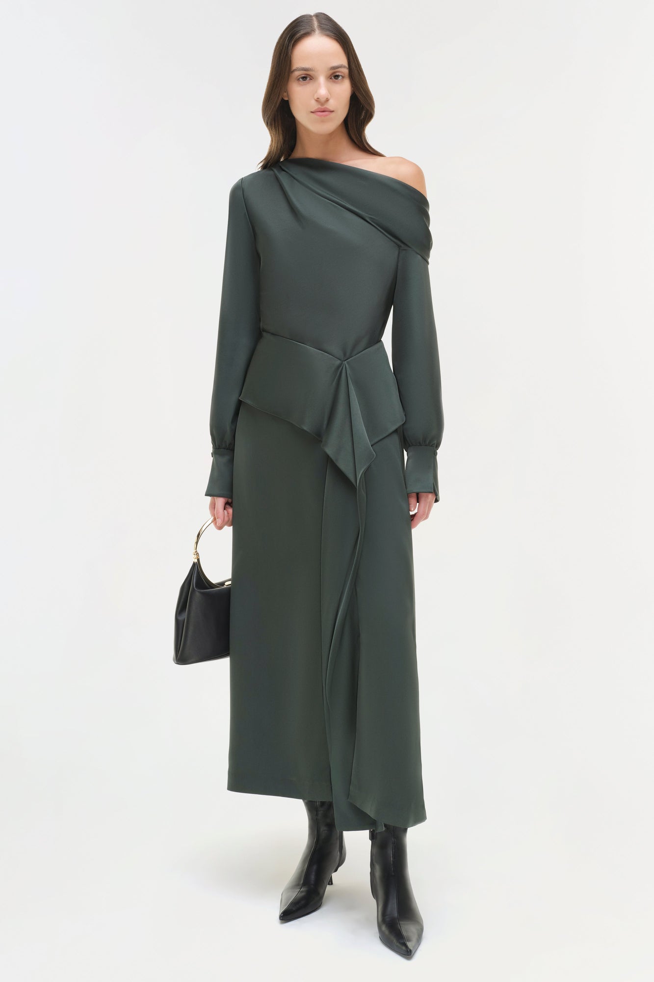 Woman wearing dark green satin midi skirt with matching off-shoulder top, tied waist detail, and black boots.