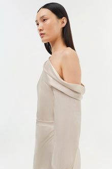 Cream-colored off-shoulder dress with draped neckline and long sleeves, shown on model in profile view.
