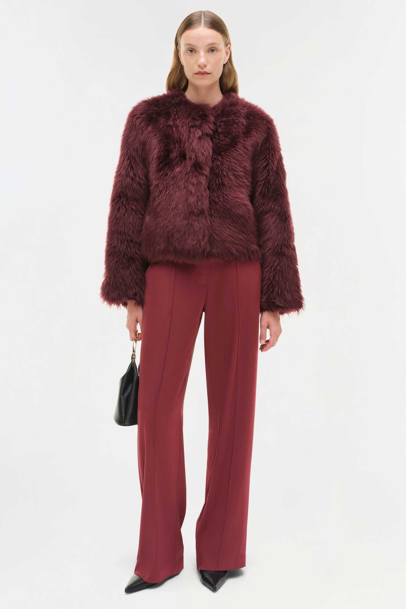 Woman wearing a burgundy shearling jacket with matching wide-leg trousers and black handbag.