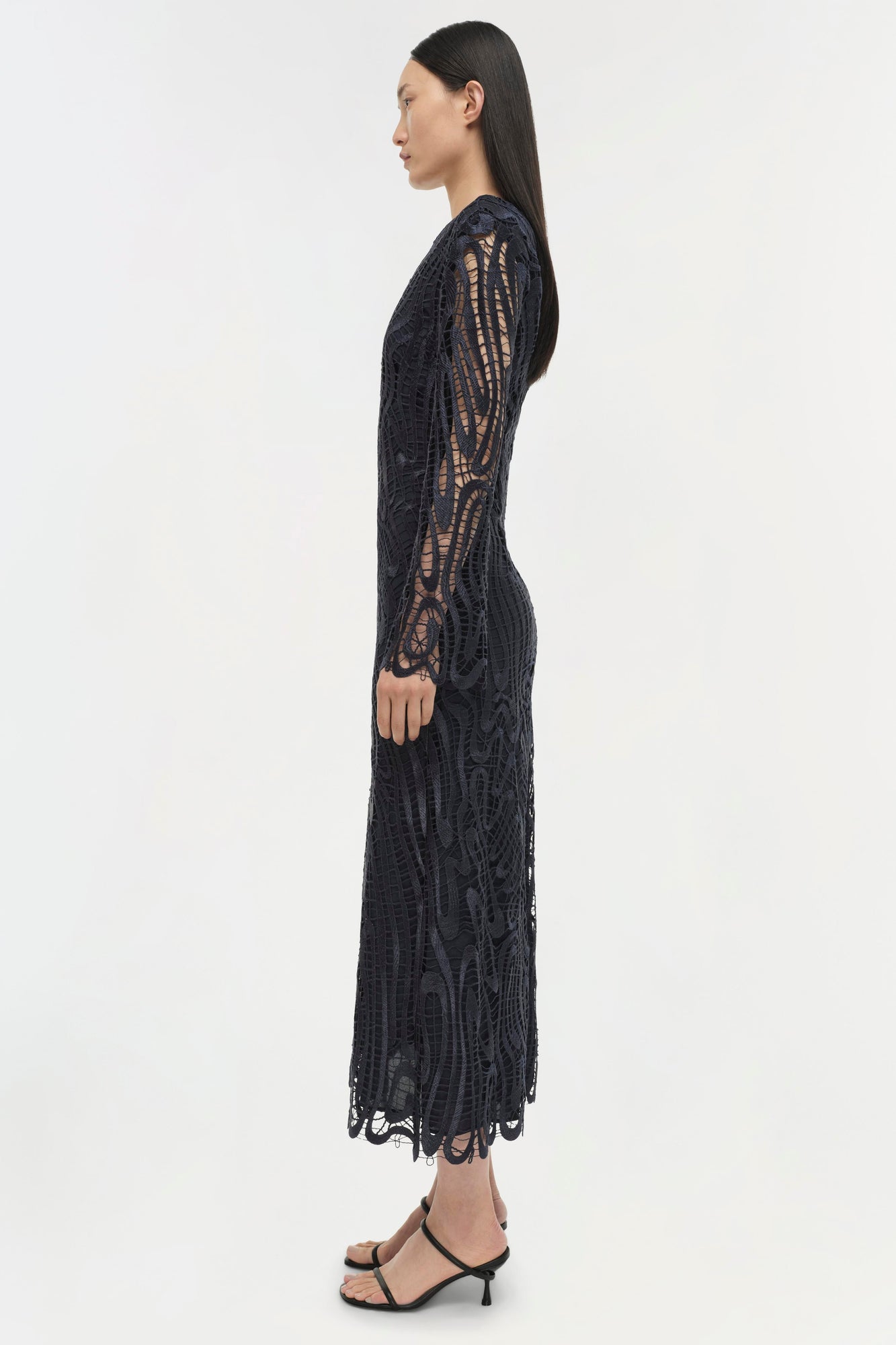 Black lace midi dress with long sleeves and cutout details, shown on model in profile view.
