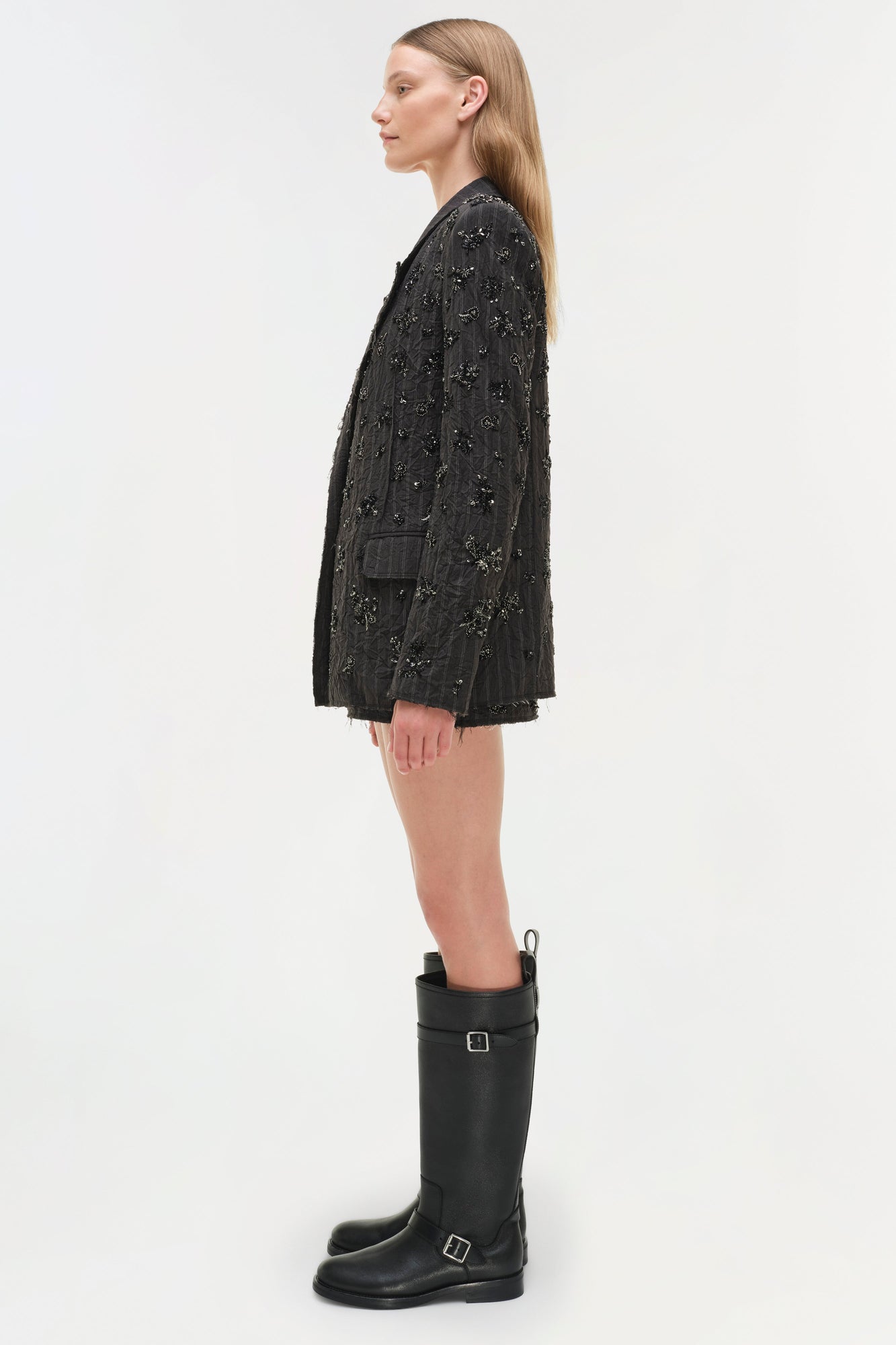 Black embellished blazer with beaded detailing worn over a black buckled knee-high boot.