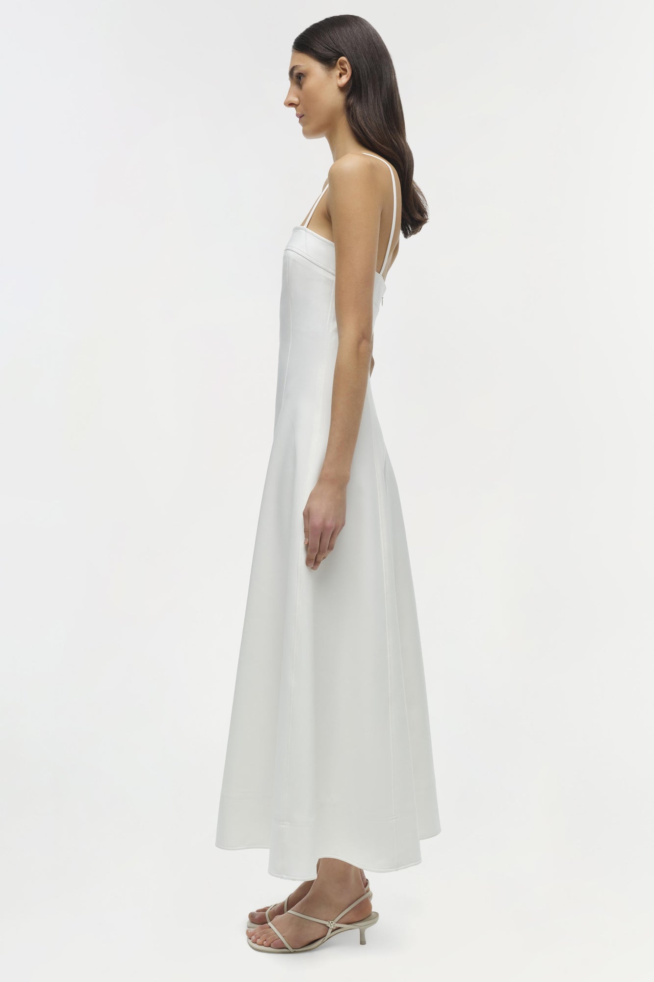 White sleeveless midi dress with thin straps, shown on model from side profile.