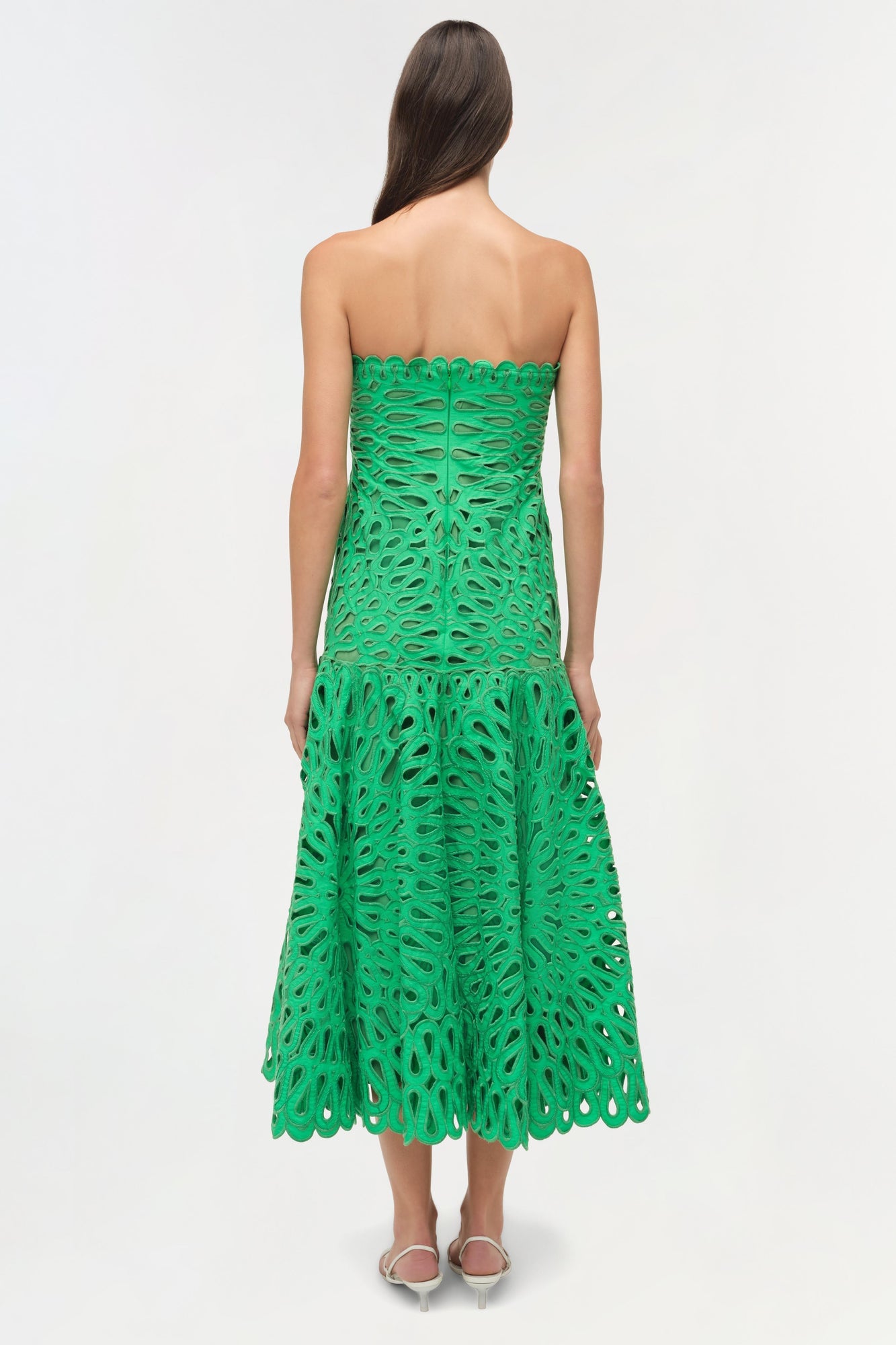 Woman wearing a green strapless midi dress with cutout embroidered details and a tiered skirt, shown from the back.
