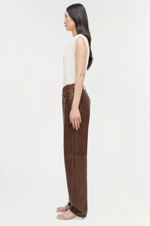 Woman wearing cream sleeveless cashmere vest over brown trousers, shown in side profile.