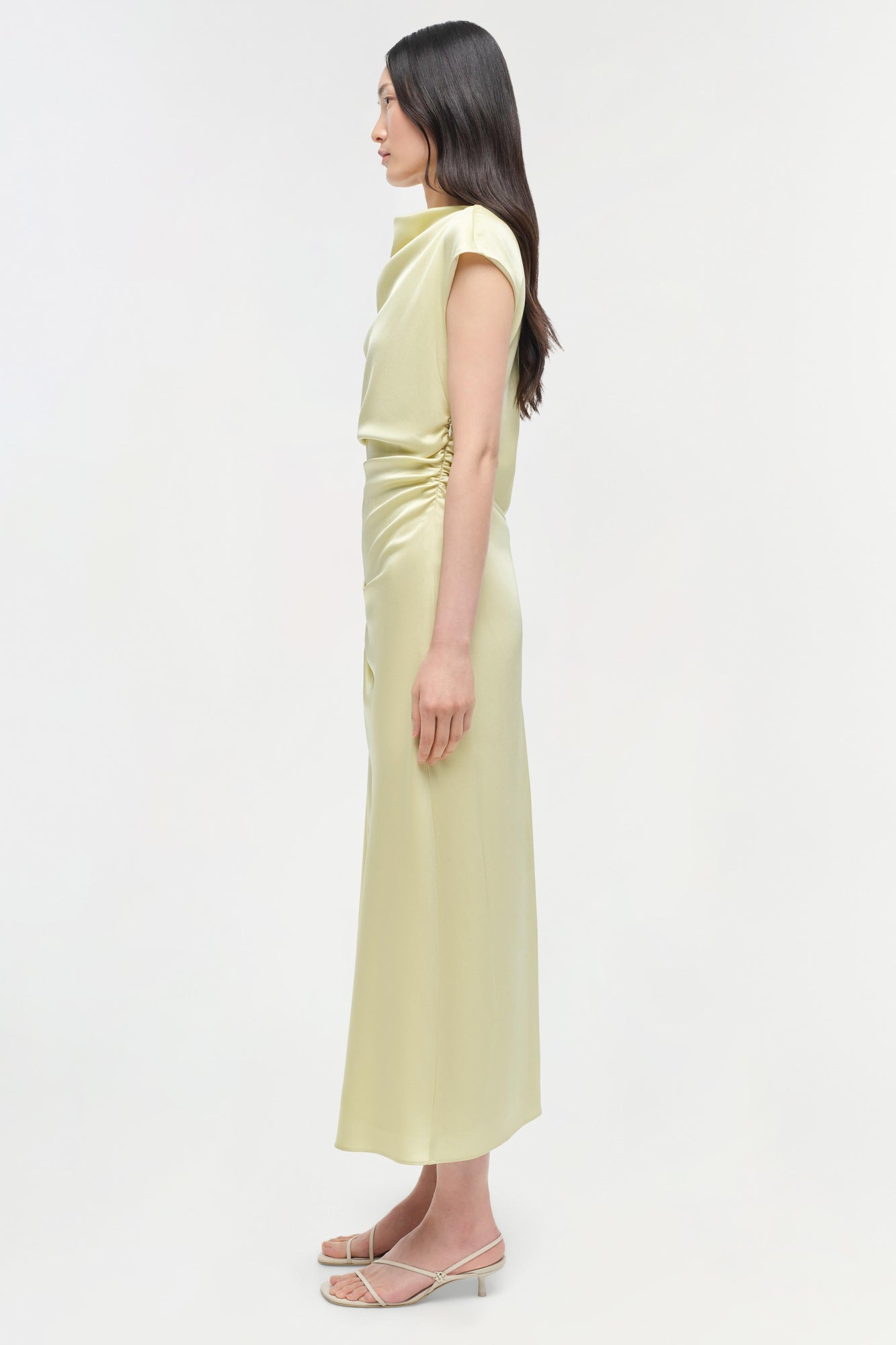 Pale yellow satin midi dress with cap sleeves and ruched side detail, shown on model from side profile.