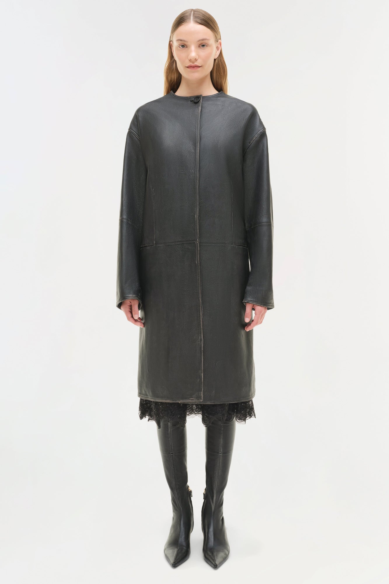 Woman wearing charcoal leather coat with lace trim hem, front zip closure, and long sleeves styled over black boots.