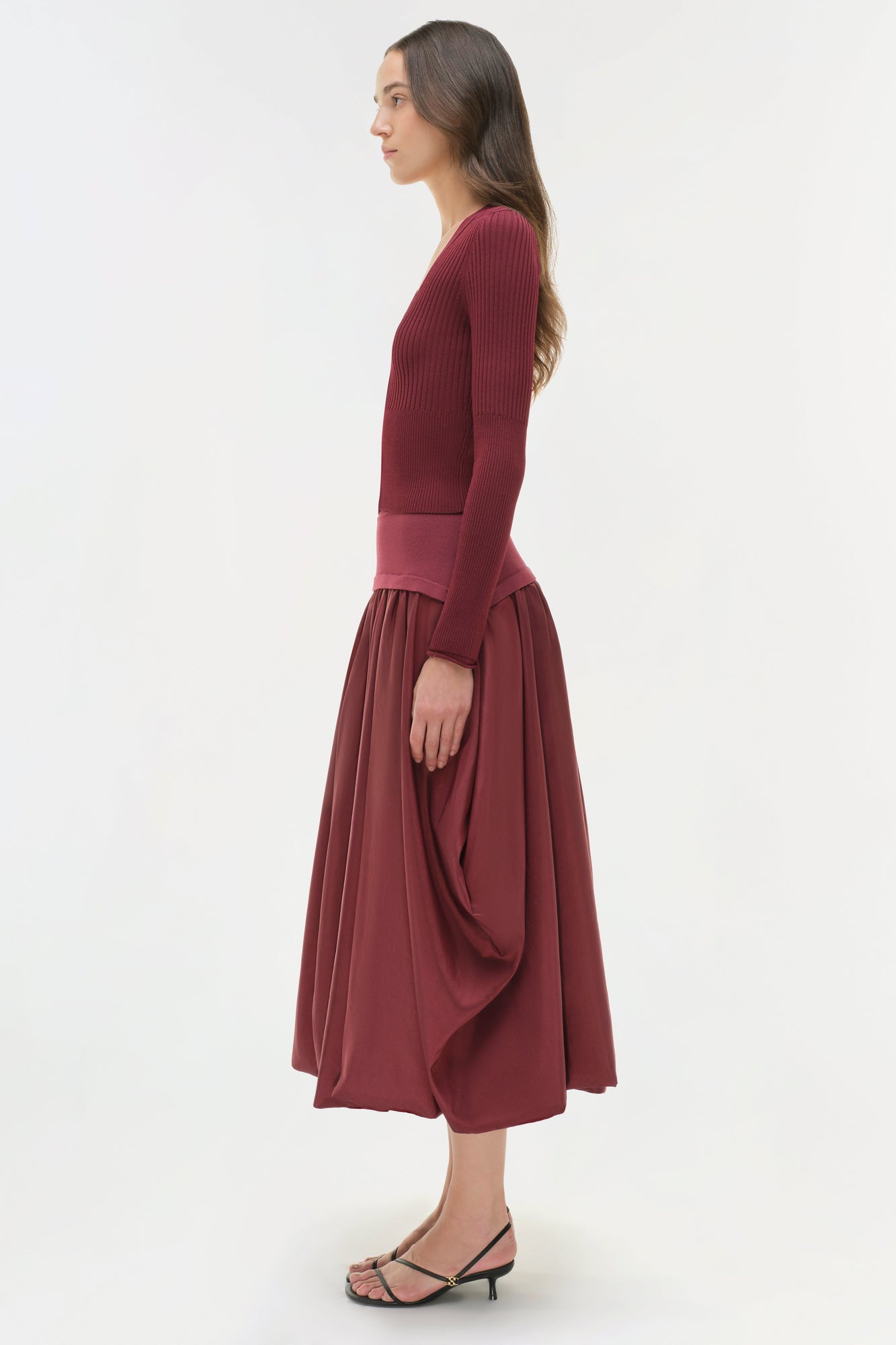 Woman wearing burgundy ribbed knit top with full midi skirt, shown in profile view.