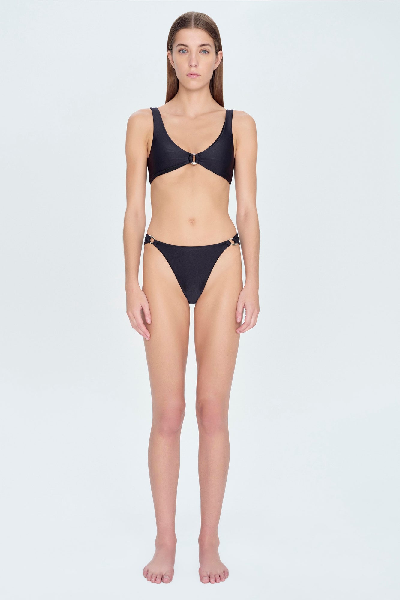 Woman wearing a black bikini top with a center ring detail and matching bikini bottom with side hardware.