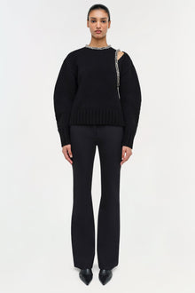Black pullover with embellished neckline and shoulder cutout detail, styled with matching black flared pants.
