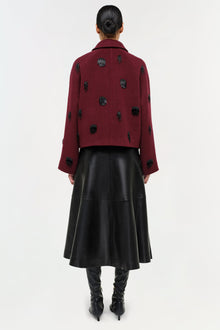 Burgundy cropped jacket with black beaded embellishments worn over black leather skirt and boots.