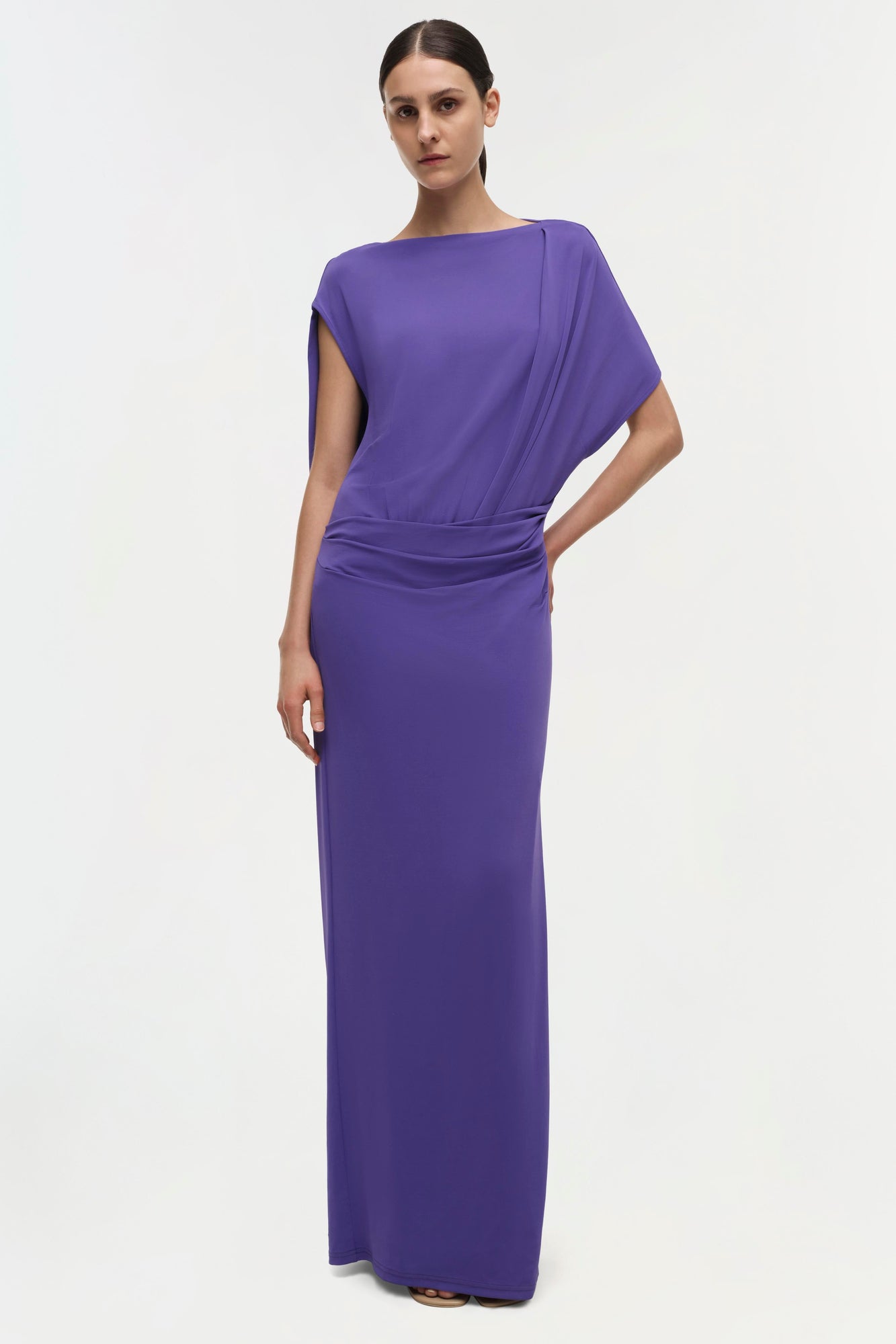 Woman wearing a purple floor-length gown with draped short sleeves and ruched waist detail.