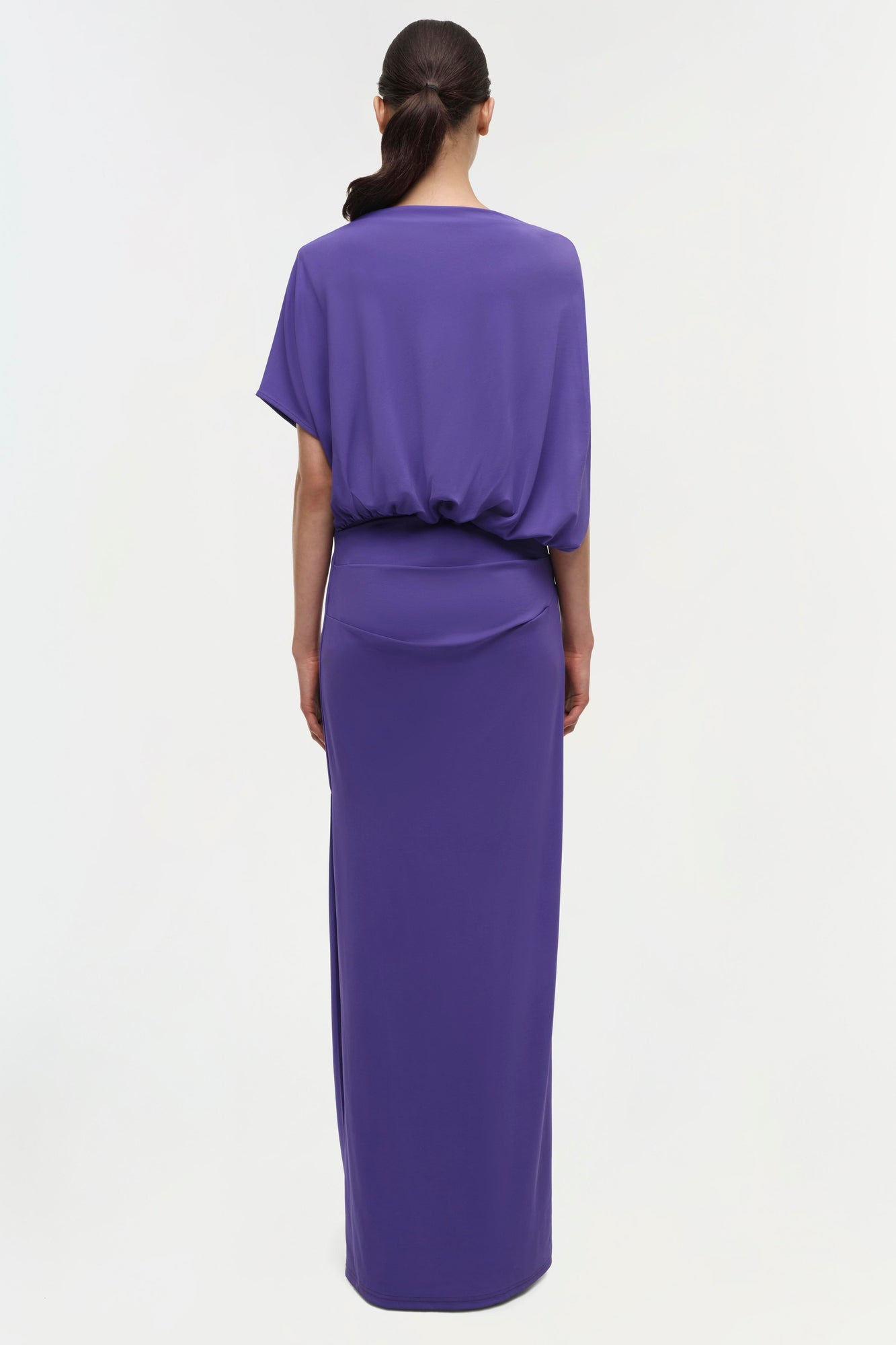 Back view of purple gown with short draped sleeves, cinched waist, and floor-length skirt.