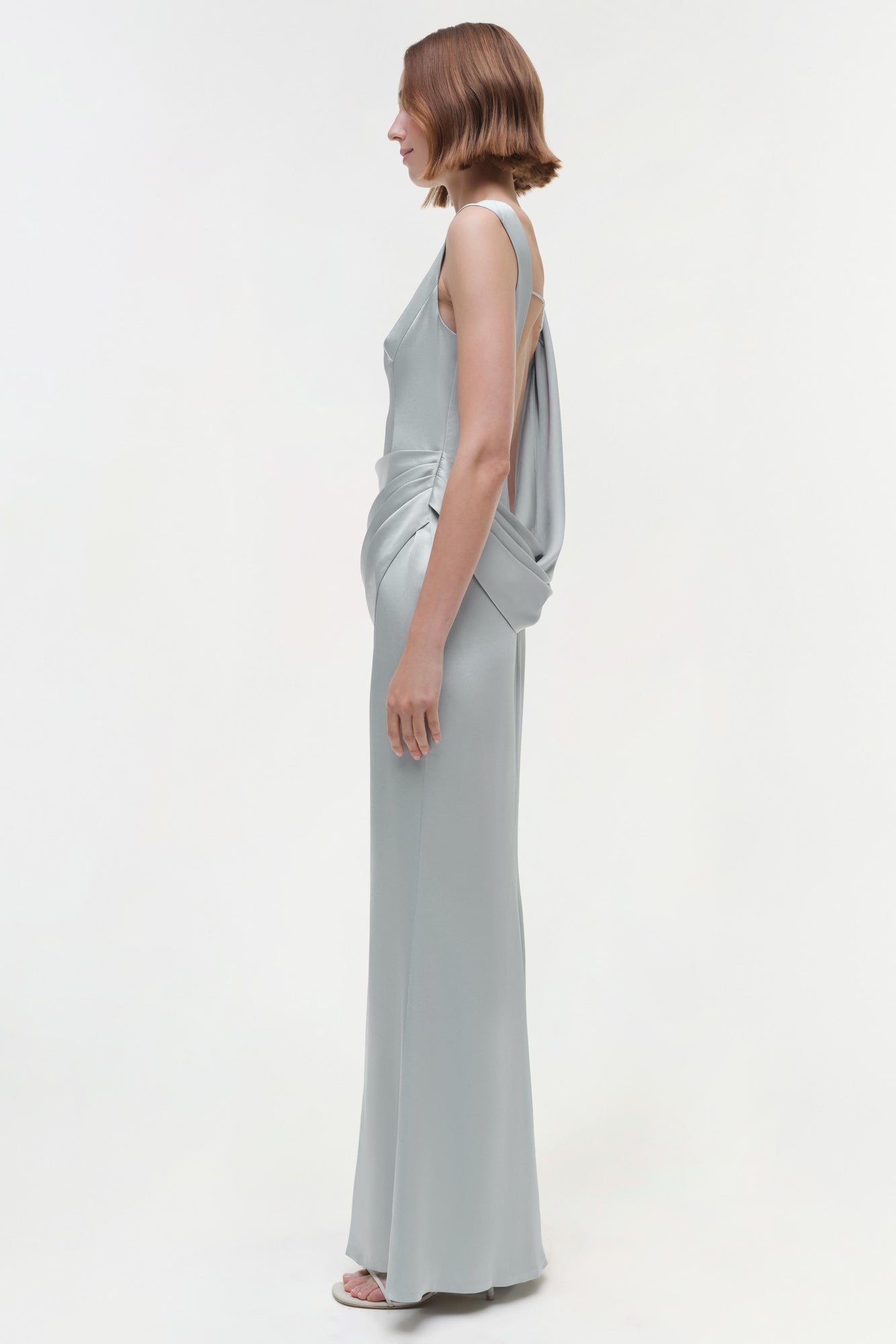 Gray sleeveless floor-length gown with draped back detail, shown from side view on model.