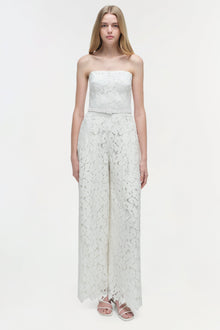 White lace strapless jumpsuit with wide legs and lace trim hem worn with white sandals.