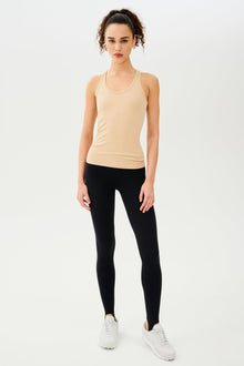 Full front view of girl wearing a yellowish brown ribbed tank top and black leggings with white shoes