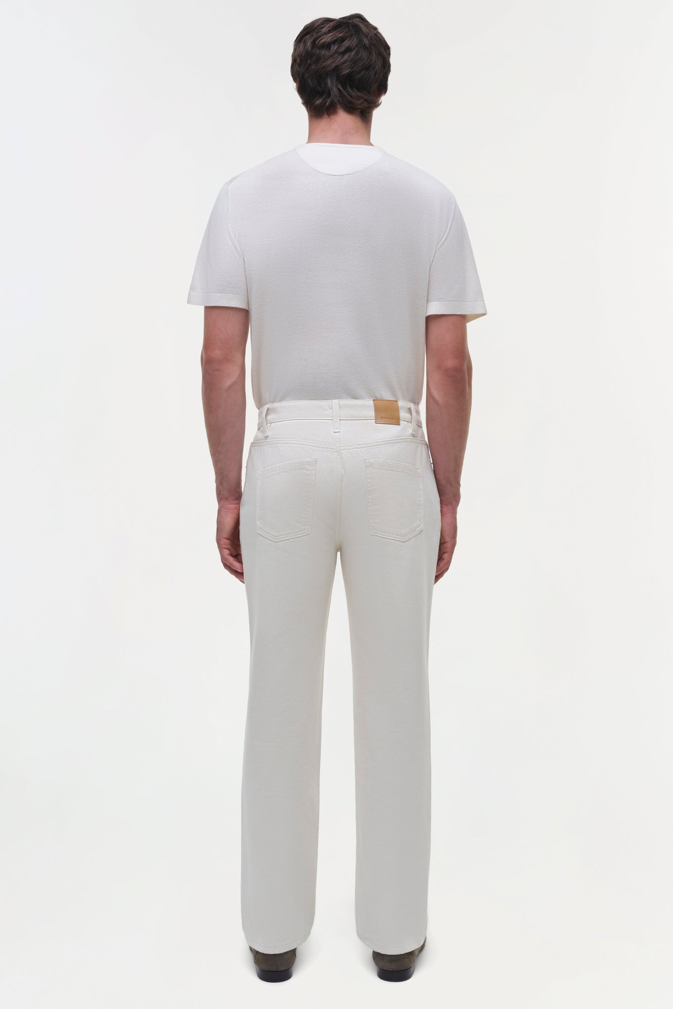 Man wearing cream-colored wide leg jeans with brown leather patch and matching short-sleeve shirt, back view.