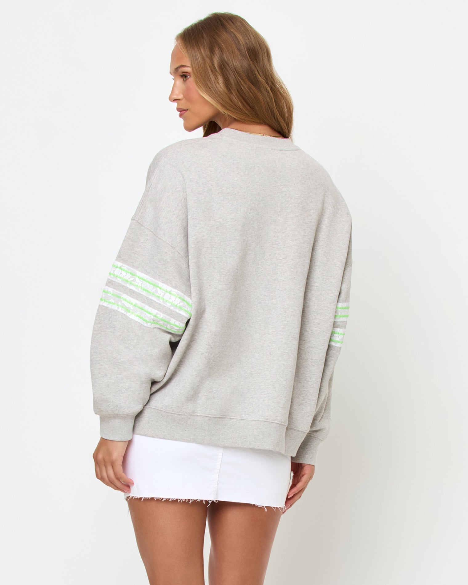 Back studio view of the Legend Sweatshirt in Limeade, a heather gray oversized crewneck sweatshirt, styled with a white denim skirt.