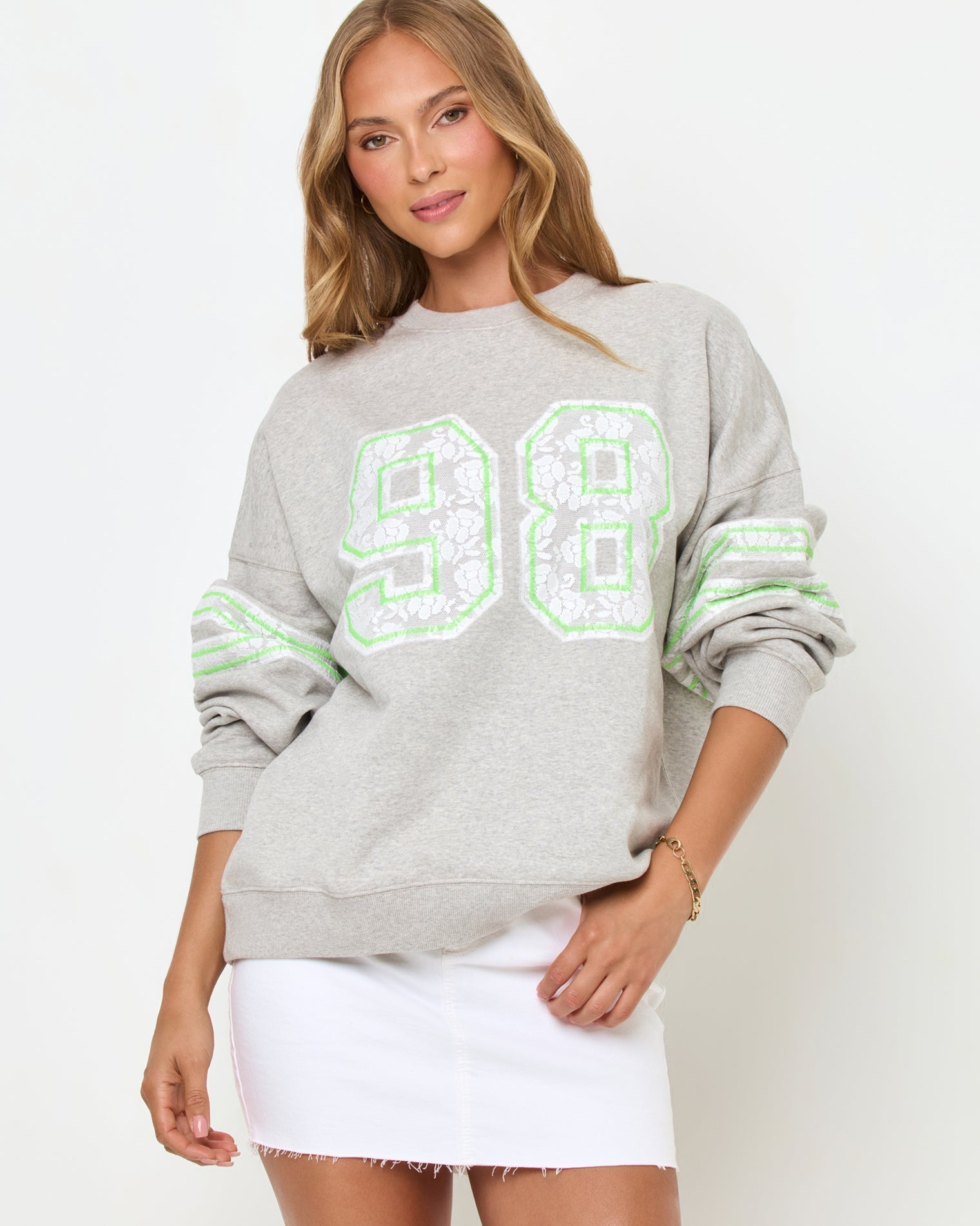 Front studio view of the Legend Sweatshirt in Limeade, a heather gray oversized crewneck sweatshirt with a neon green "98" graphic on the chest, styled with a white denim skirt.