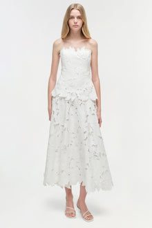 White strapless midi dress with leaf-shaped embroidered details throughout, worn with white strappy sandals.