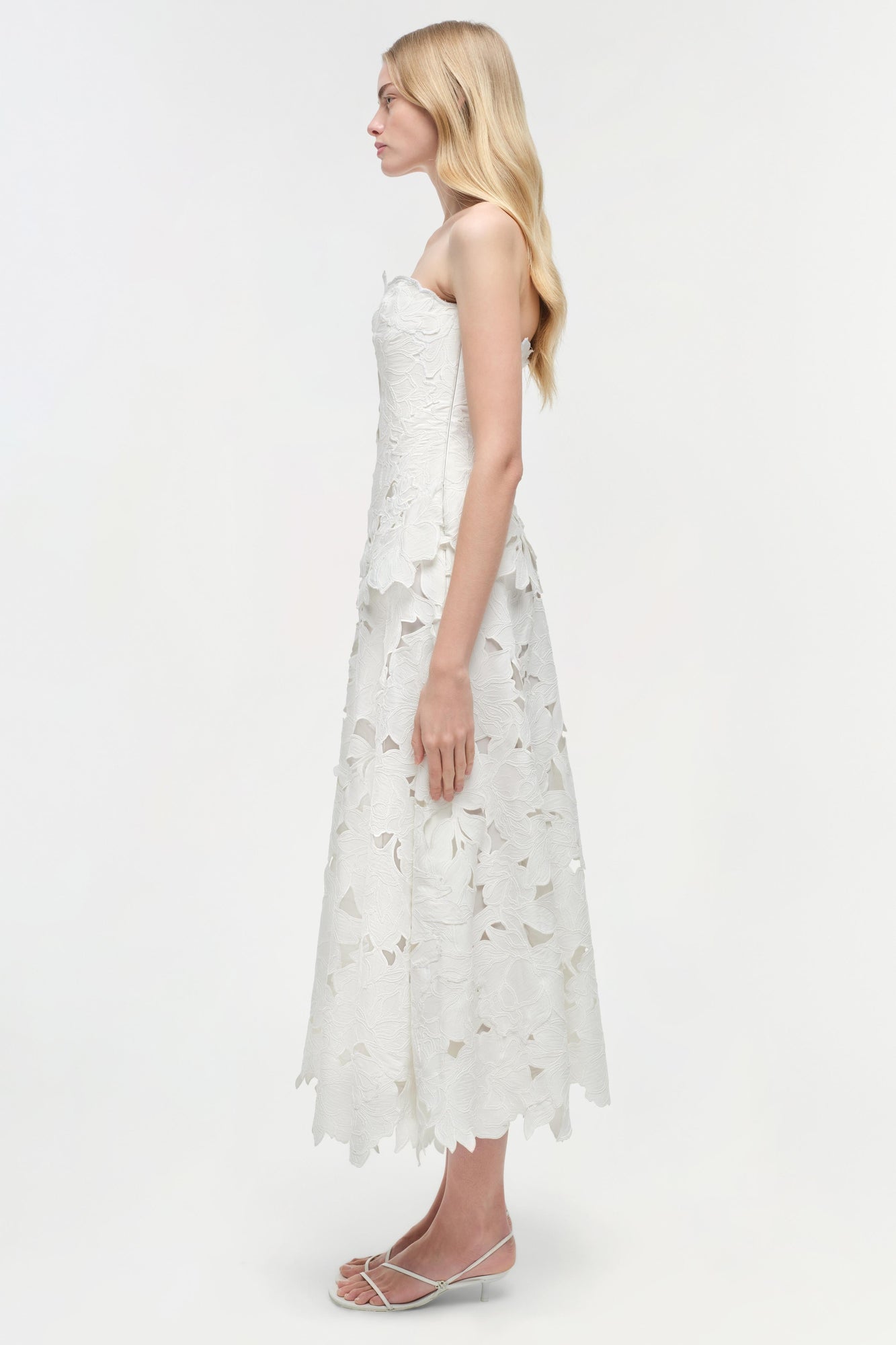 White sleeveless midi dress with floral embroidered cutout pattern, shown on model in side profile view.
