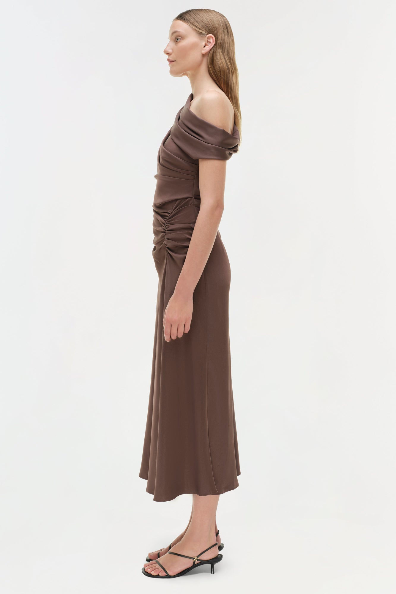 Woman wearing a taupe satin off-shoulder midi dress with ruched side detailing and thin straps.