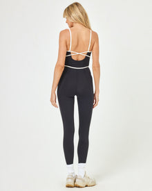 Back view of model wearing the Ace Jumpsuit in black-cream showing the open back and cream contrast piping detail.