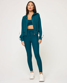 Front view of model wearing the Back To Back Jacket in deep teal-cream with matching deep teal-cream Back To Back Pant and white sneakers.
