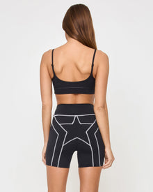 Back view of the LSPACE Eclipse Bra in black on a model against a white background, showing the back strap detail, paired with matching black-cream active shorts.