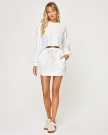 Front view of model wearing the Half Court Skirt in white, a ribbed drawstring mini skirt, with matching white Half Court Pullover and white sneakers with red accent.