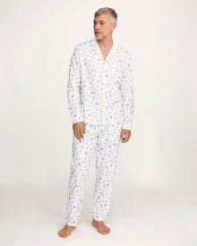A man with short gray hair wears the Men's Twill Pajama Set in Easter Frolic—white pants and a long-sleeve top with a small, colorful print—standing barefoot against a plain light background.