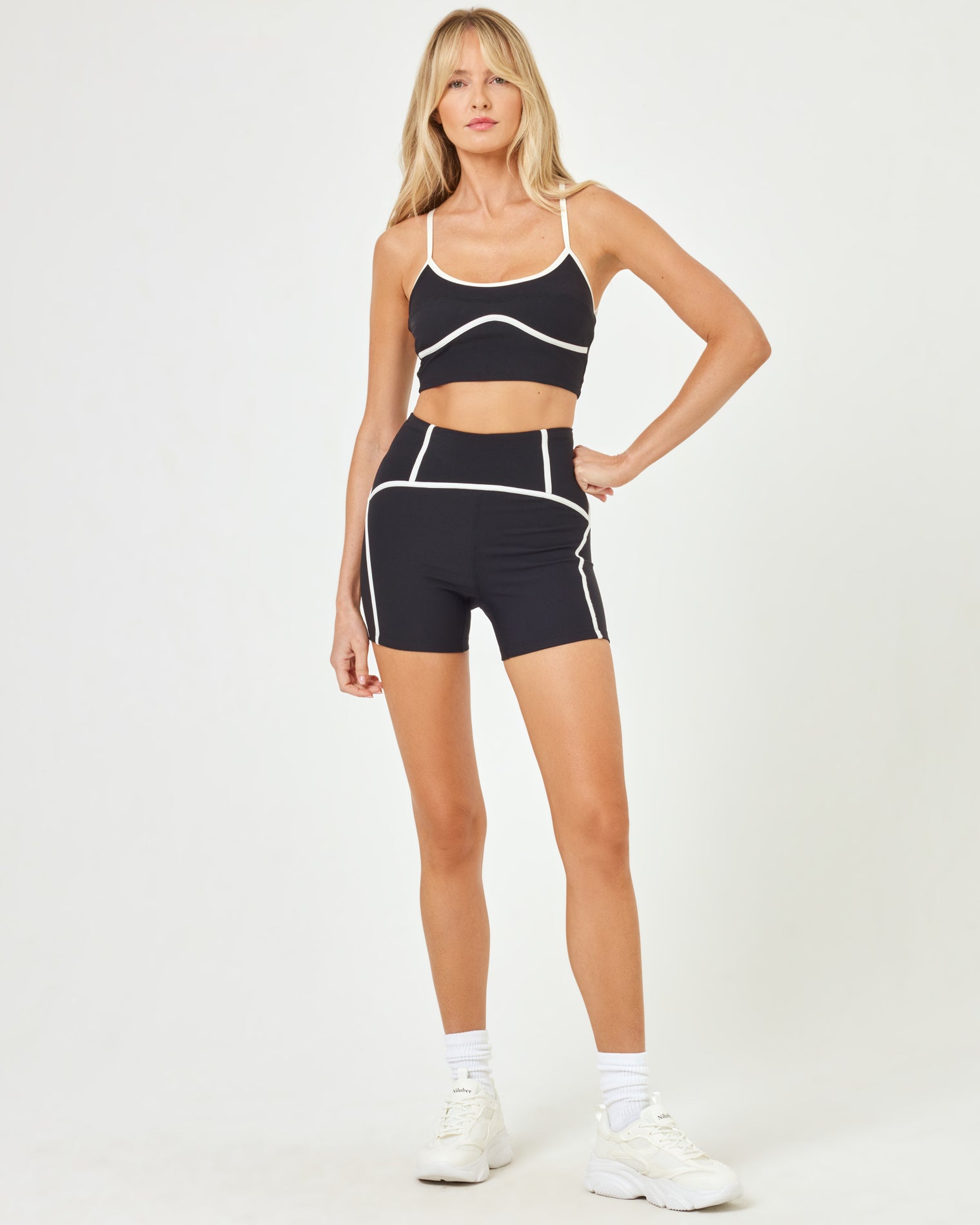 Front view of model wearing the Revel Short in black-cream with matching black-cream Revel Top and white sneakers.