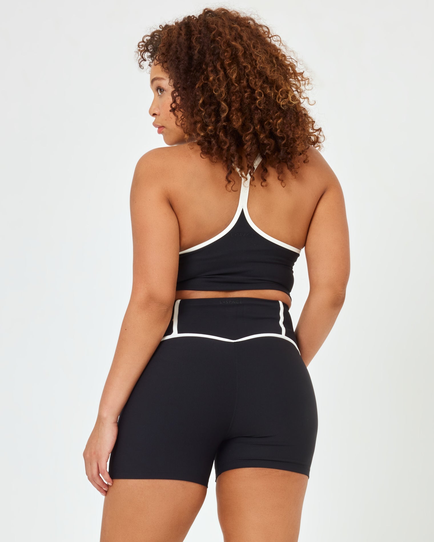 Back view of plus size model wearing the Revel Top in black-cream showing the crossback strap detail with cream piping, with matching black-cream Revel Short.