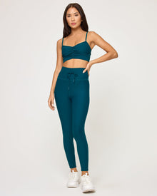Front view of model wearing the Soren Top in deep teal with matching deep teal Turner Legging and white sneakers.