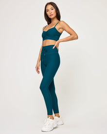 Side view of model wearing the Soren Top in deep teal with matching deep teal Turner Legging and white sneakers.