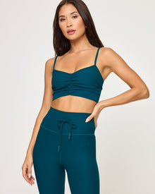 Close-up front view of model wearing the Soren Top in deep teal, a ruched sweetheart crop top with spaghetti straps, with matching deep teal Turner Legging with drawstring waist, hand on hip.